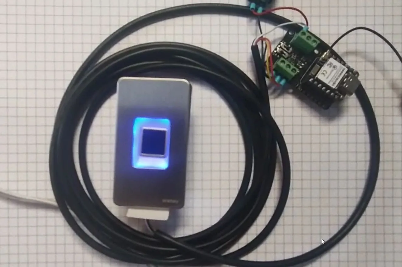 A fingerprint scanner with its illuminated sensor window, a coiled RS485 cable, and a small XIAO board on an RS485 expansion board with screw terminals.